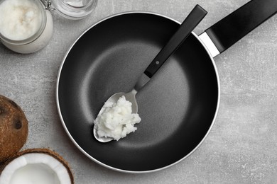 Photo of Frying pan with coconut oil and spoon on light grey table, flat lay