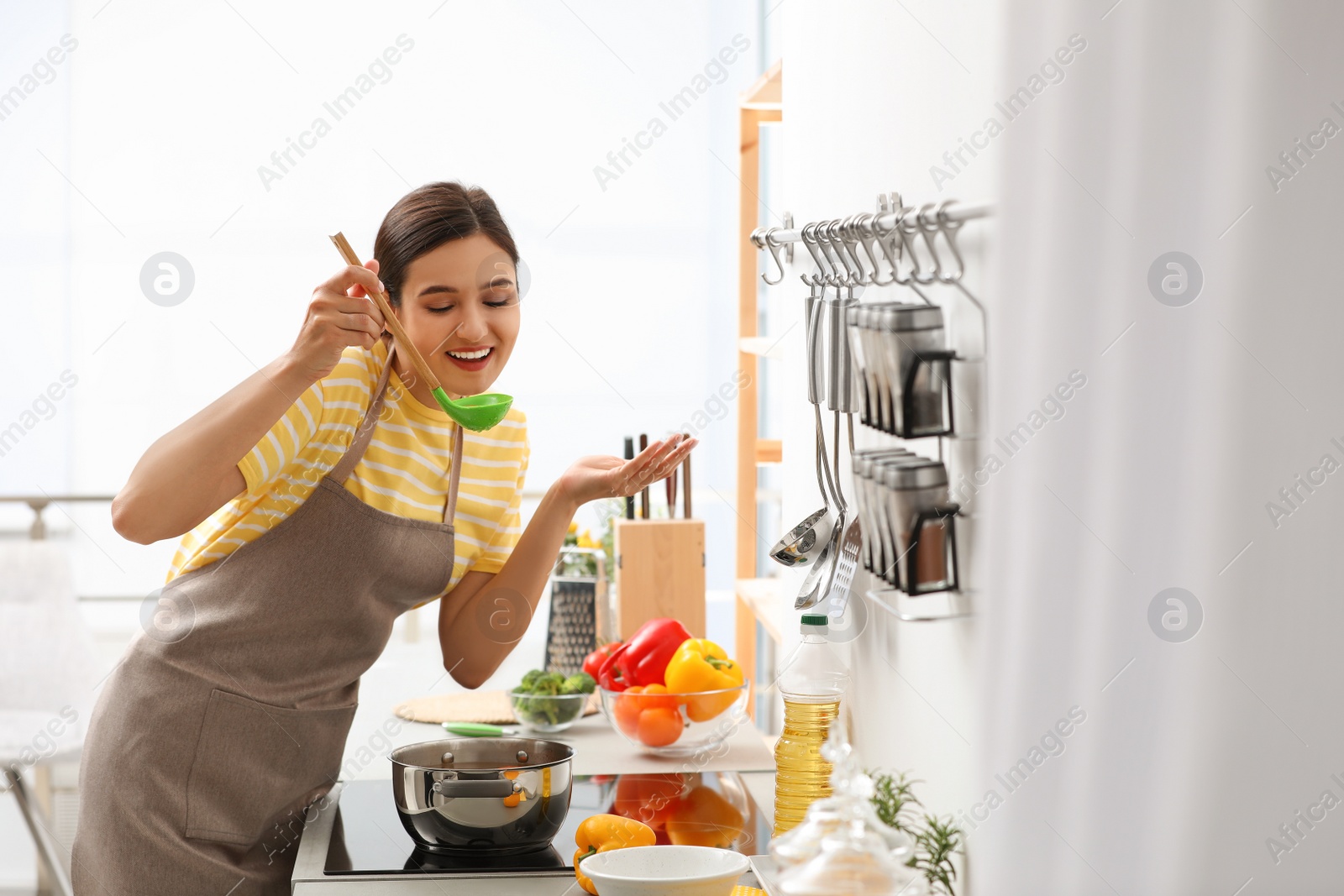 Photo of Young woman cooking tasty soup in kitchen