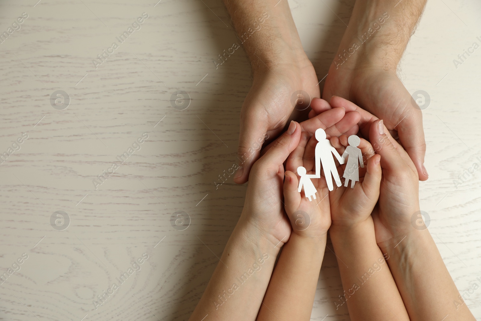 Photo of Parents and child holding paper cutout of family at white wooden table, top view. Space for text