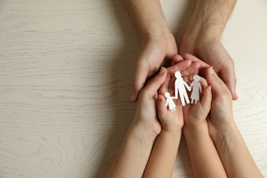 Photo of Parents and child holding paper cutout of family at white wooden table, top view. Space for text