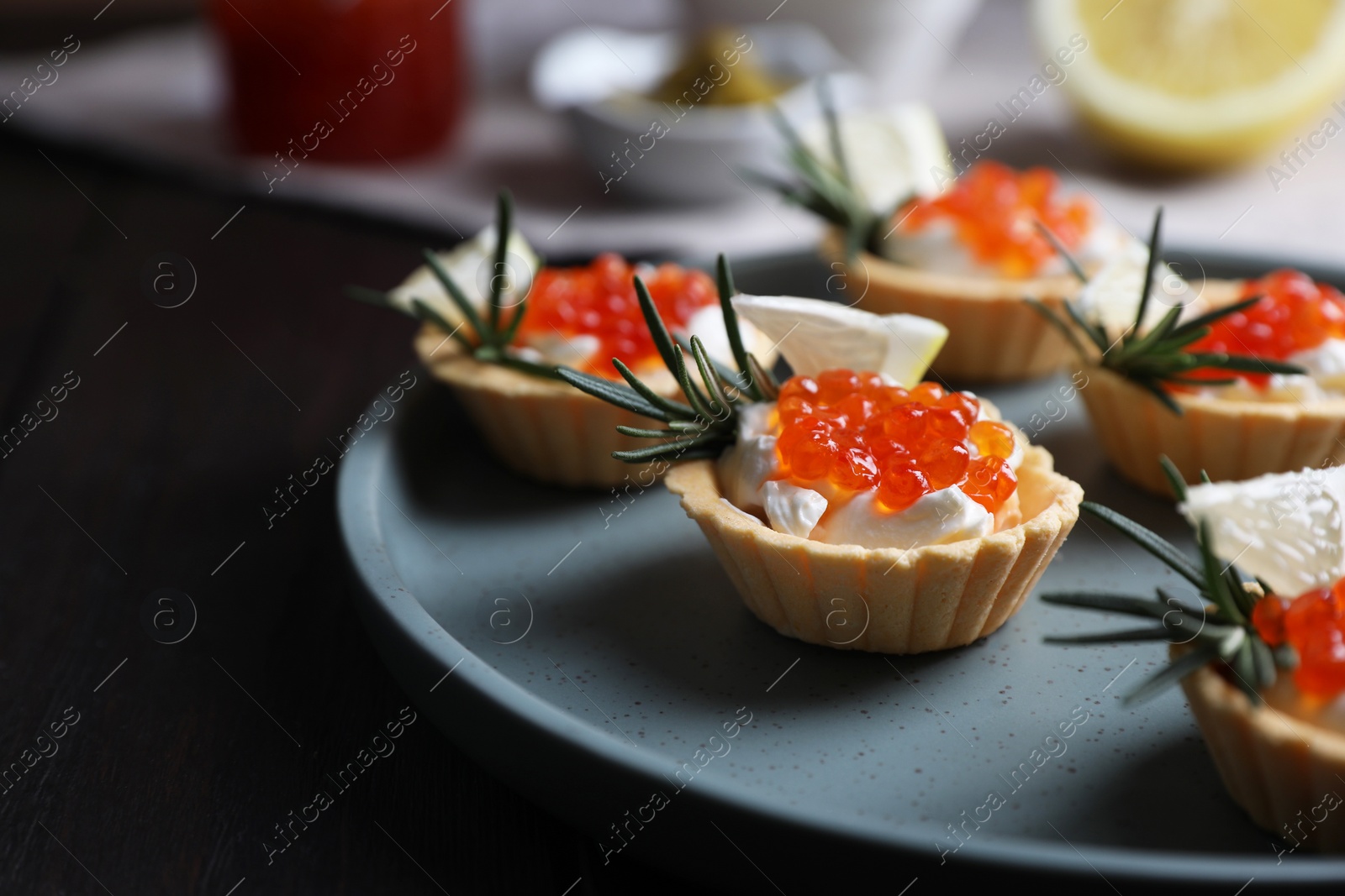 Photo of Delicious tartlets with red caviar and cream cheese served on wooden table, closeup