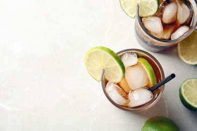 Photo of Glasses of cocktail with cola, ice and cut lime on light background, flat lay. Space for text