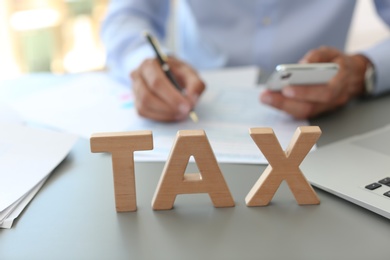 Photo of Word TAX and blurred accountant on background