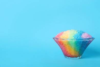 Photo of Rainbow shaving ice in glass dessert bowl on light blue background, space for text