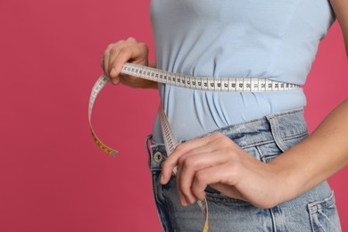 Woman measuring waist with tape on pink background, closeup