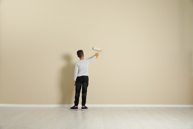 Photo of Child painting color wall with roller brush. Space for text