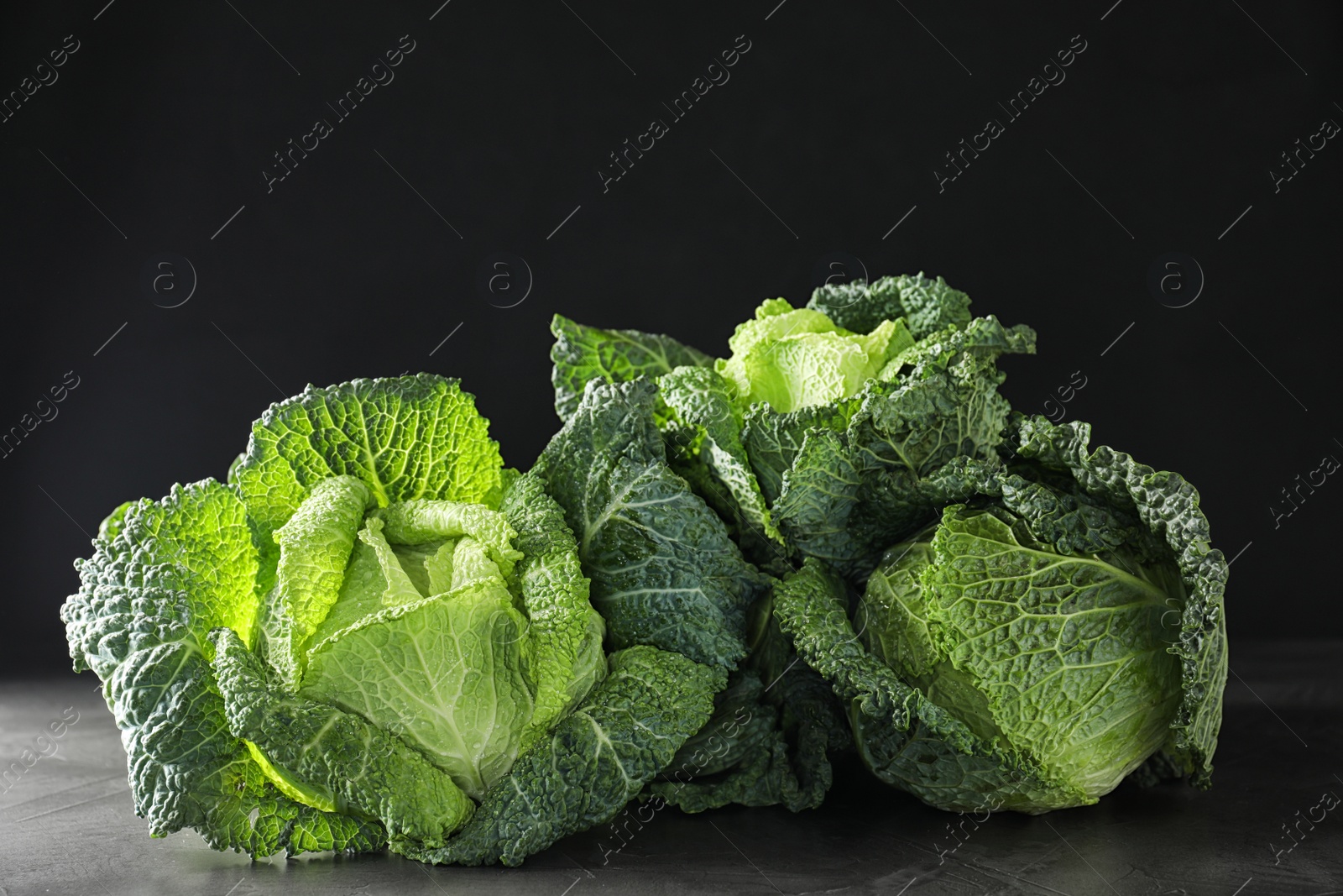 Photo of Fresh green savoy cabbages on grey table against black background