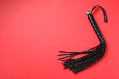 Photo of Black whip on red background, top view with space for text. Sexual role play accessory