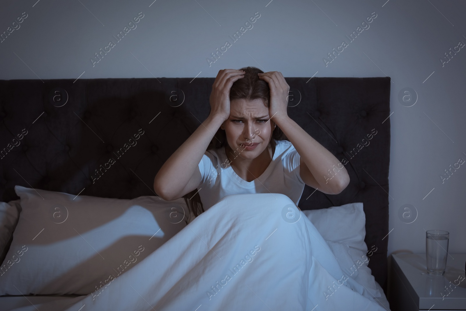 Photo of Young woman with terrible headache sitting in bed at night
