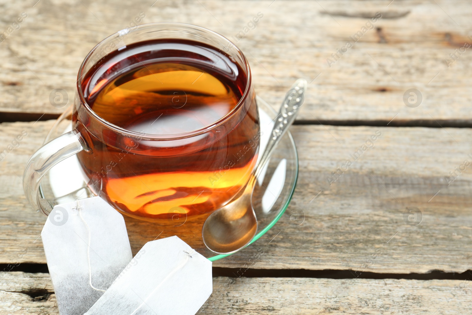 Photo of Aromatic tea in glass cup, spoon and teabags on wooden table. Space for text