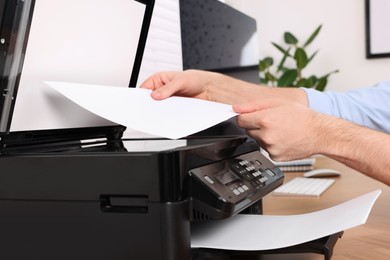 Photo of Man using modern printer at wooden table indoors, closeup