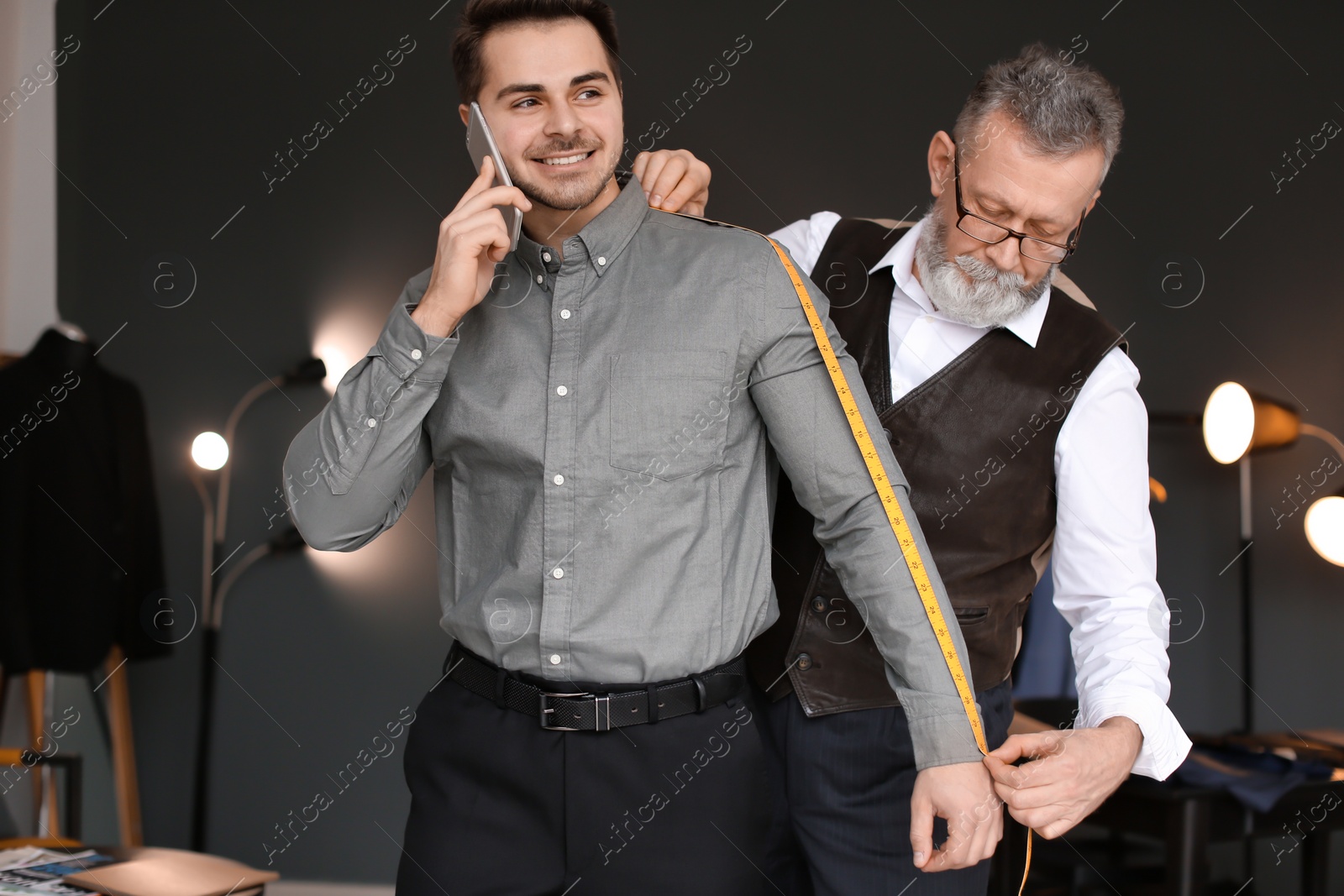 Photo of Mature tailor taking client's measurements in atelier