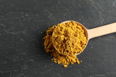 Photo of Spoon with dry curry powder on dark textured table, top view. Space for text