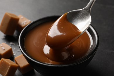 Photo of Taking yummy salted caramel with spoon from bowl on table, closeup