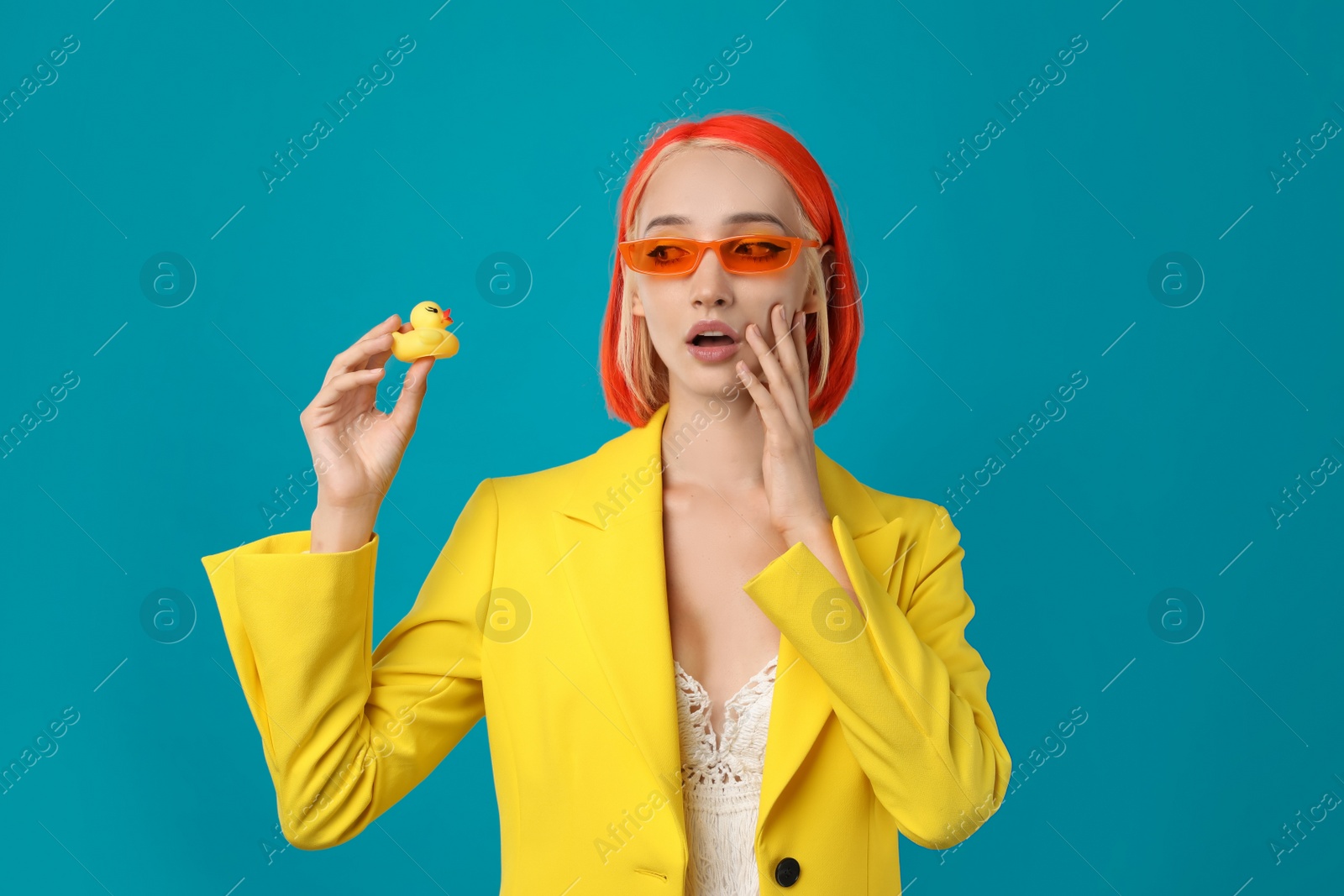 Photo of Emotional young woman with bright dyed hair and toy duck on turquoise background