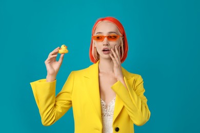 Emotional young woman with bright dyed hair and toy duck on turquoise background