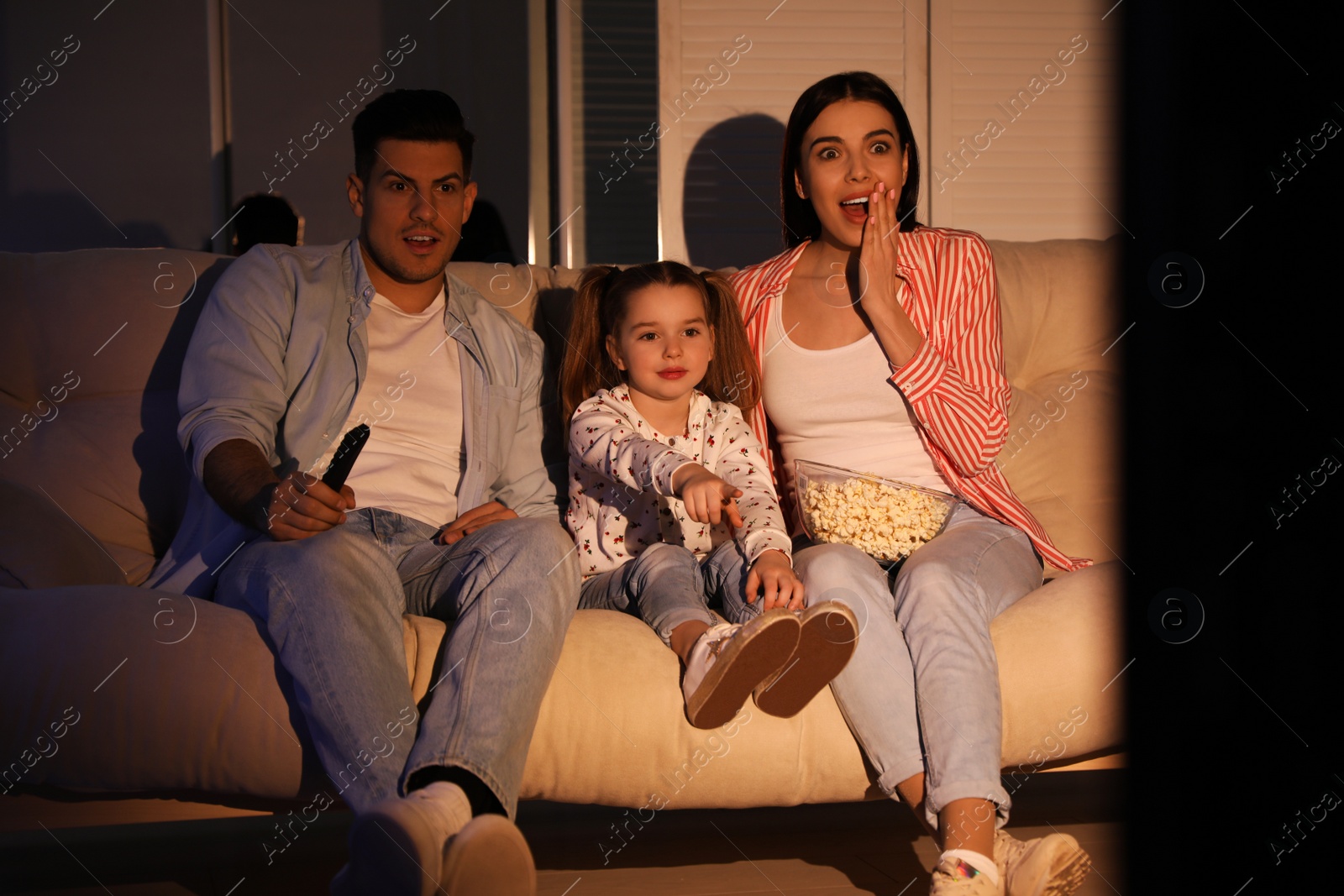 Photo of Family watching movie with popcorn on sofa at night