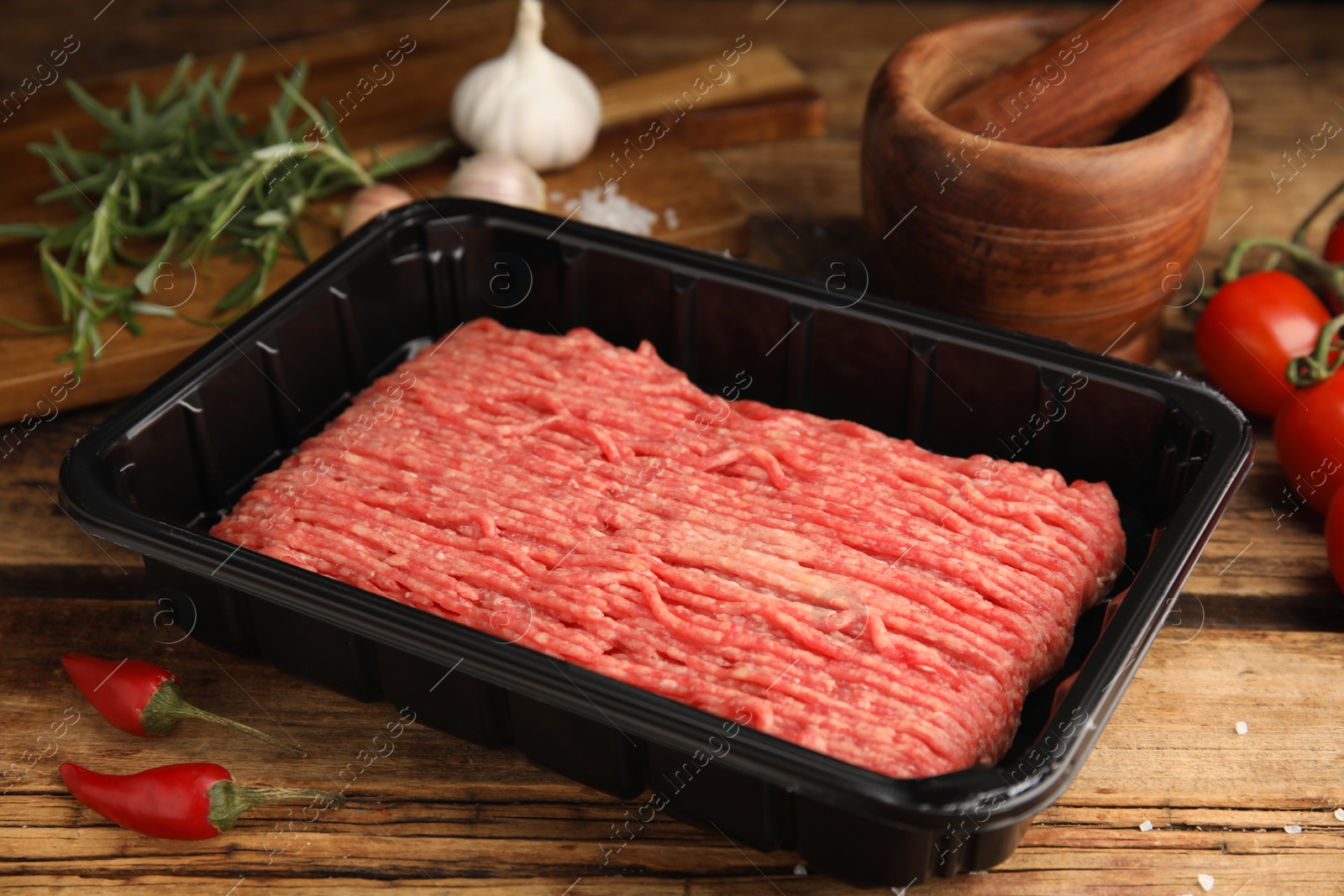 Photo of Raw fresh minced meat in plastic container and other ingredients on wooden table