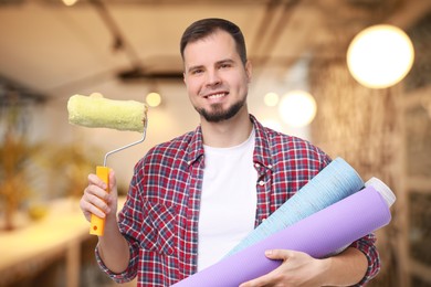 Man with wallpaper roll and roller on blurred background