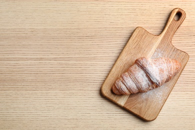 Photo of Wooden board with fresh croissant, powdered sugar and space for text on wooden background, top view. French pastry