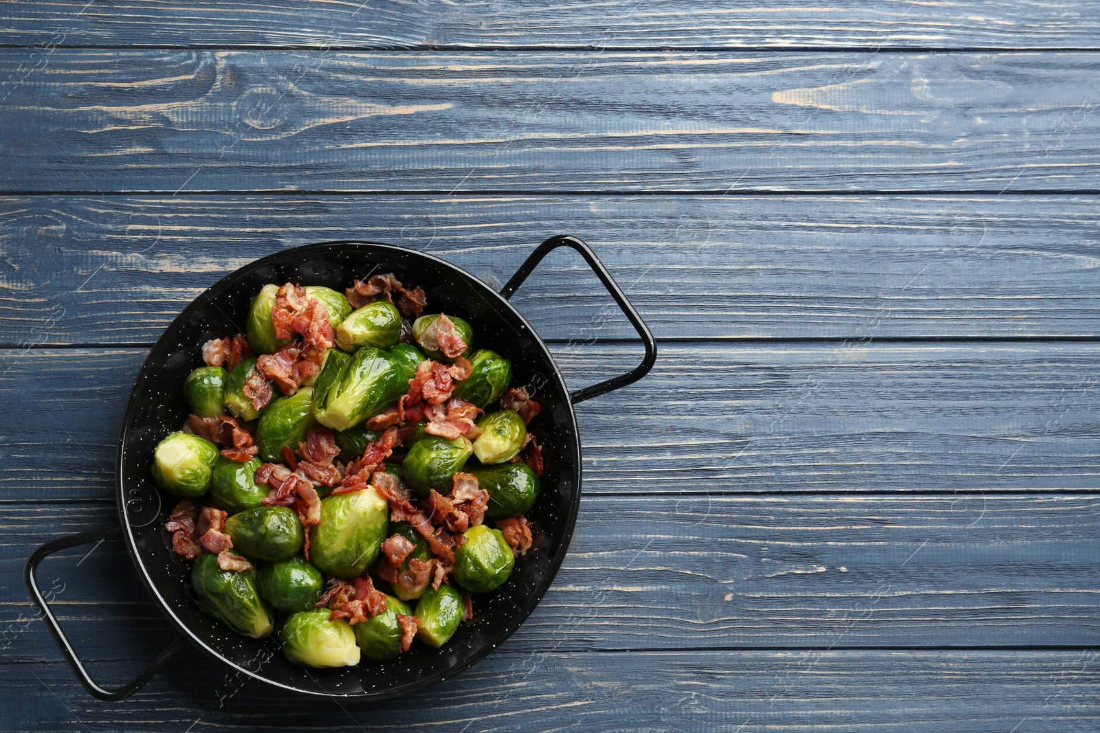 Photo of Tasty roasted Brussels sprouts with bacon on blue wooden table, top view. Space for text