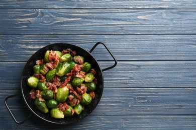 Tasty roasted Brussels sprouts with bacon on blue wooden table, top view. Space for text