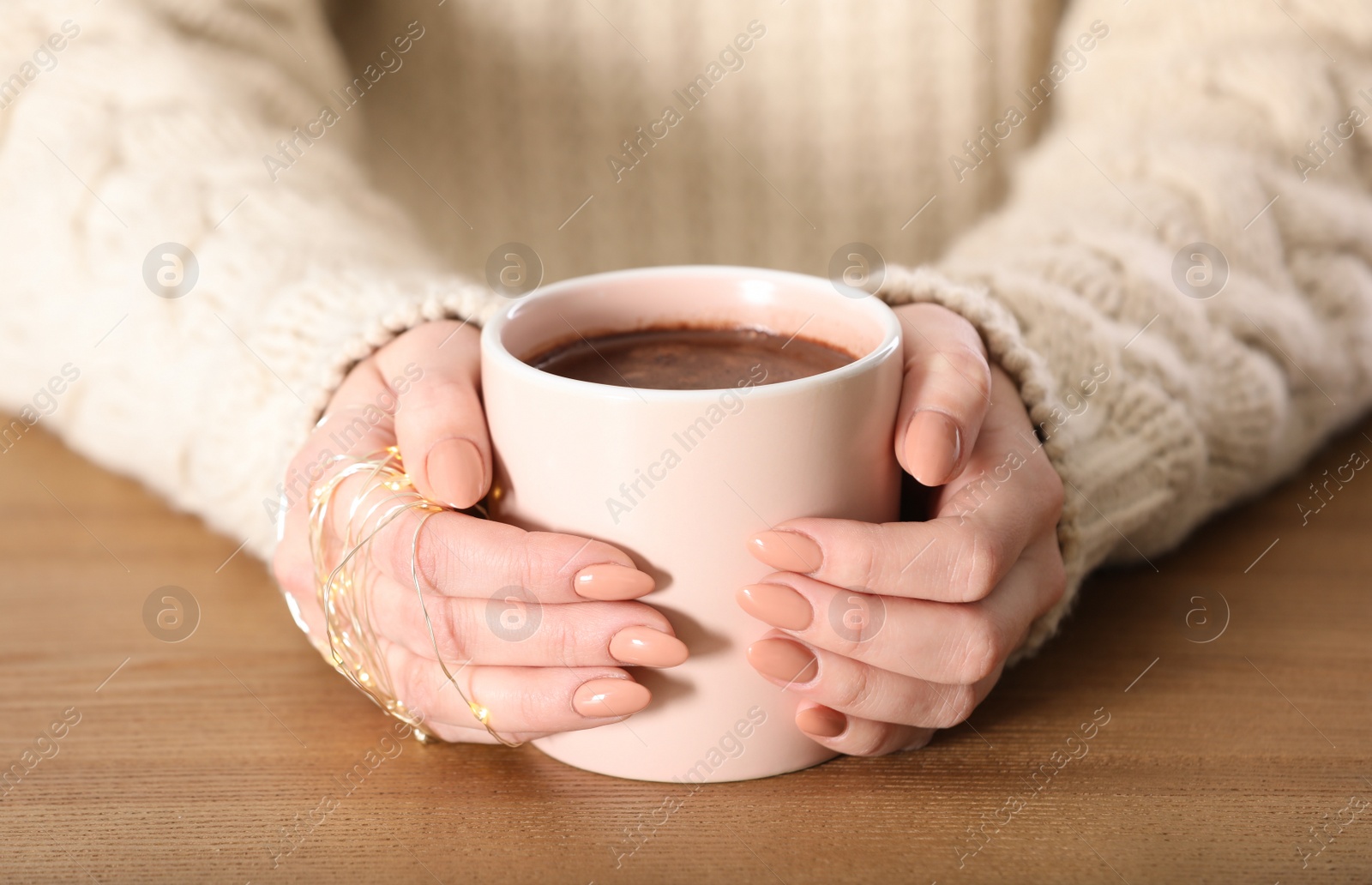 Photo of Woman in sweater holding cup of aromatic cacao on wooden table, closeup