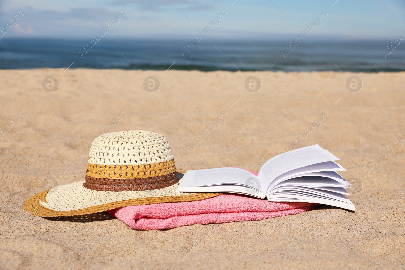 Photo of Open book, hat and pink towel on sandy beach near sea. Space for text