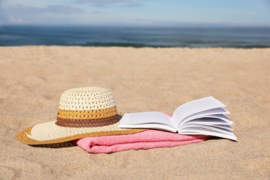 Open book, hat and pink towel on sandy beach near sea. Space for text
