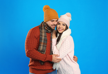 Happy young couple in warm clothes on blue background. Winter vacation