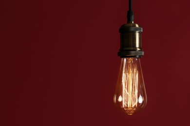 Pendant lamp with light bulb against dark red background, space for text