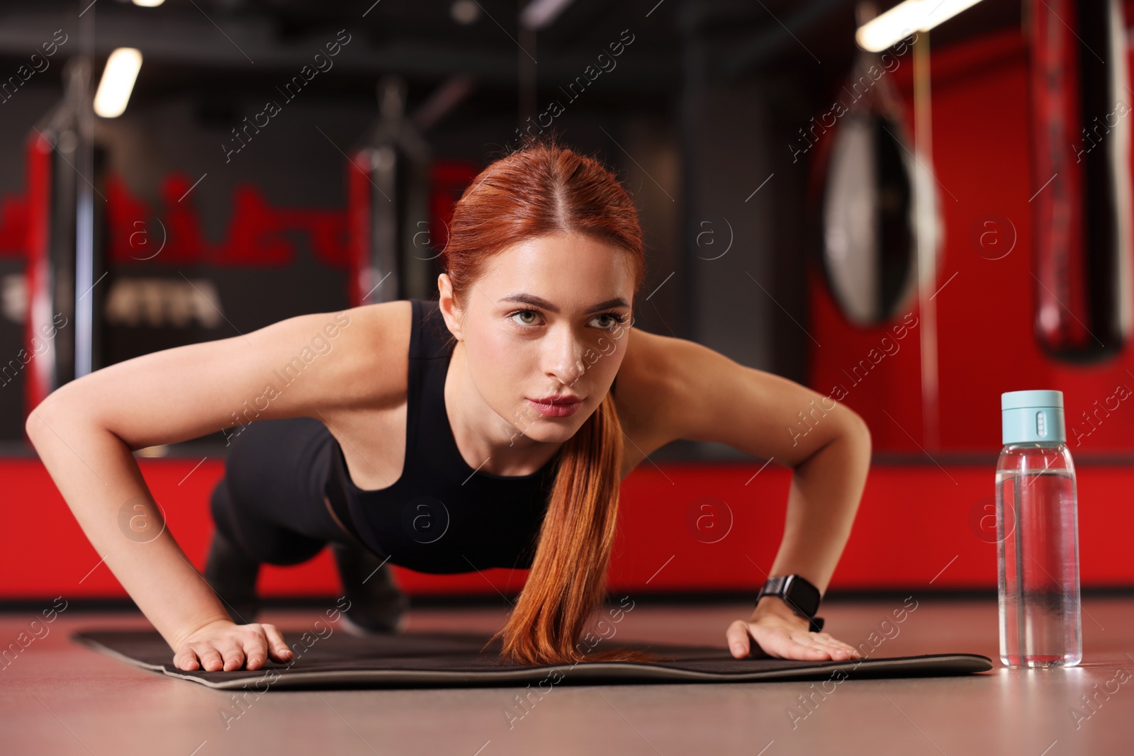 Photo of Athletic young woman doing push ups on mat in gym