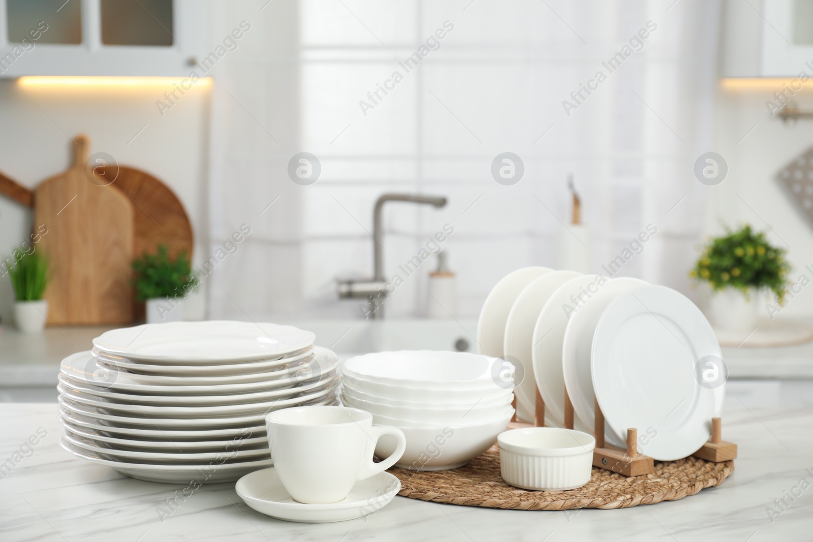 Photo of Clean plates, bowls and cup on white marble table in kitchen