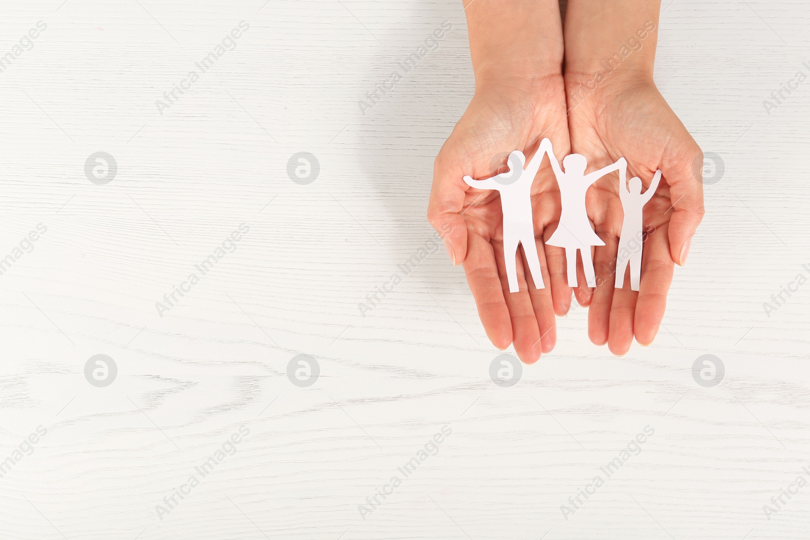 Photo of Woman holding paper figures of happy family in hands on white wooden background, top view. Space for text