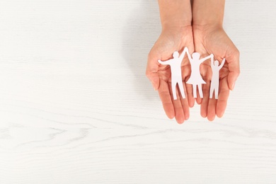 Woman holding paper figures of happy family in hands on white wooden background, top view. Space for text