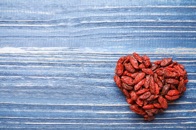 Photo of Heart shaped pile of dried goji berries on blue wooden background, top view. Space for text