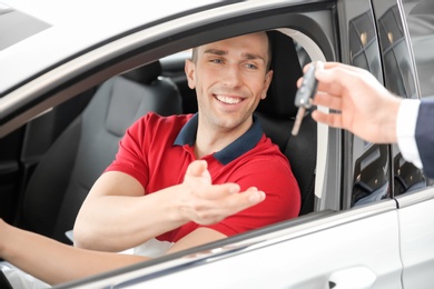 Salesman passing key to young man in auto at dealership. Buying new car