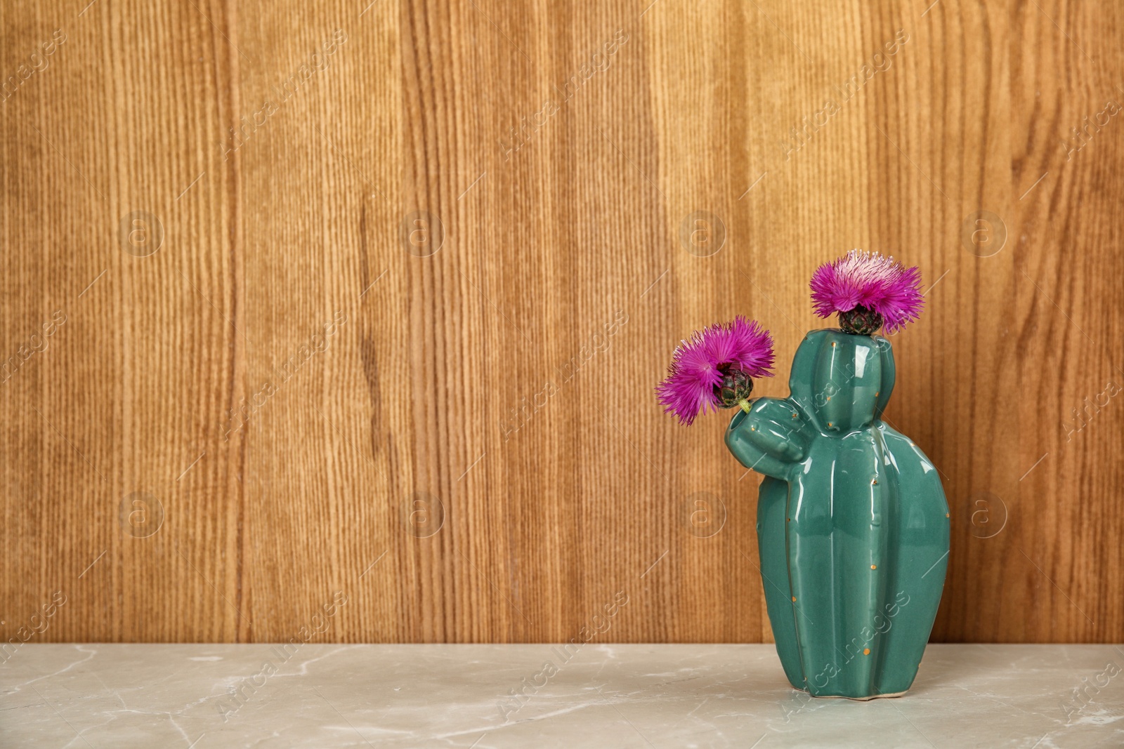 Photo of Trendy cactus shaped ceramic vase with flowers on table against wooden background