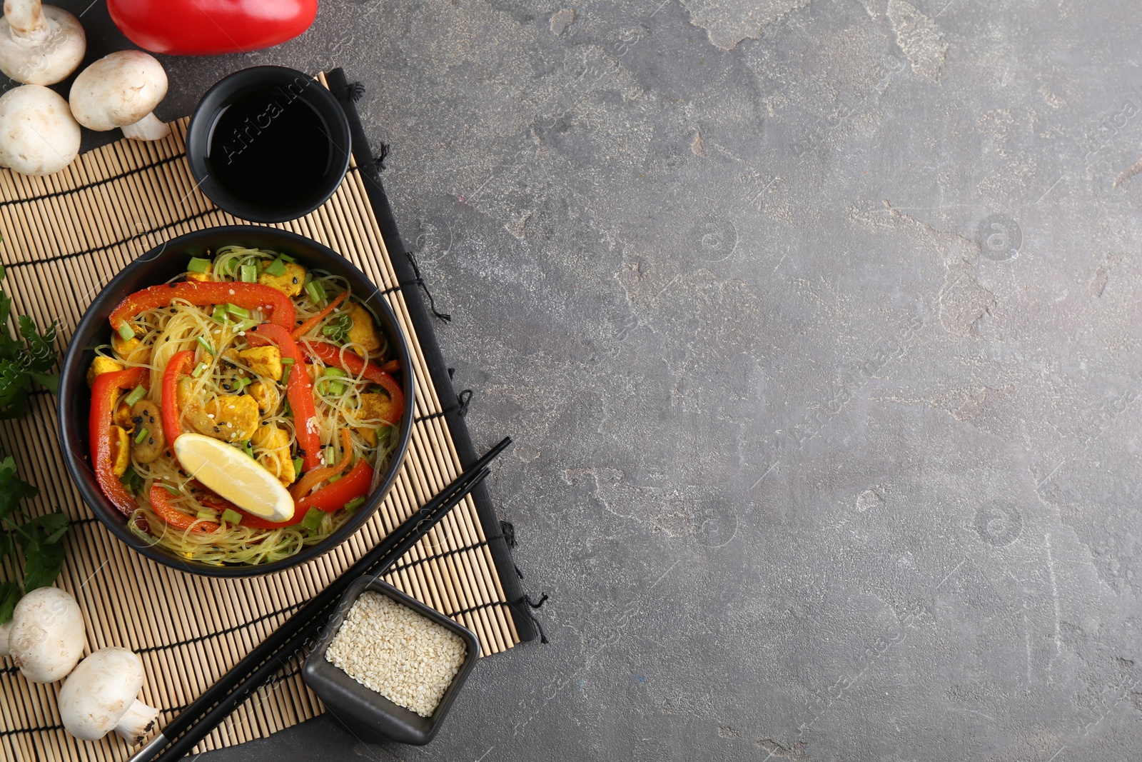 Photo of Stir-fry. Delicious cooked noodles with chicken and vegetables in bowl served on gray textured table, flat lay. Space for text