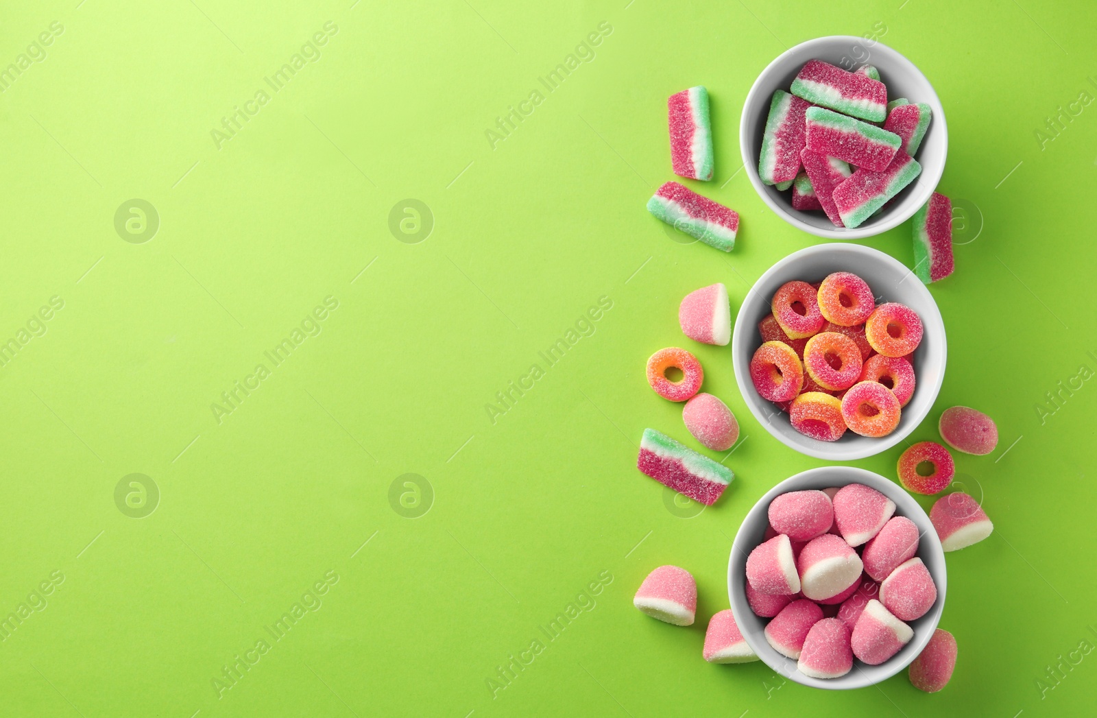 Photo of Flat lay composition with bowls of different jelly candies on green background. Space for text