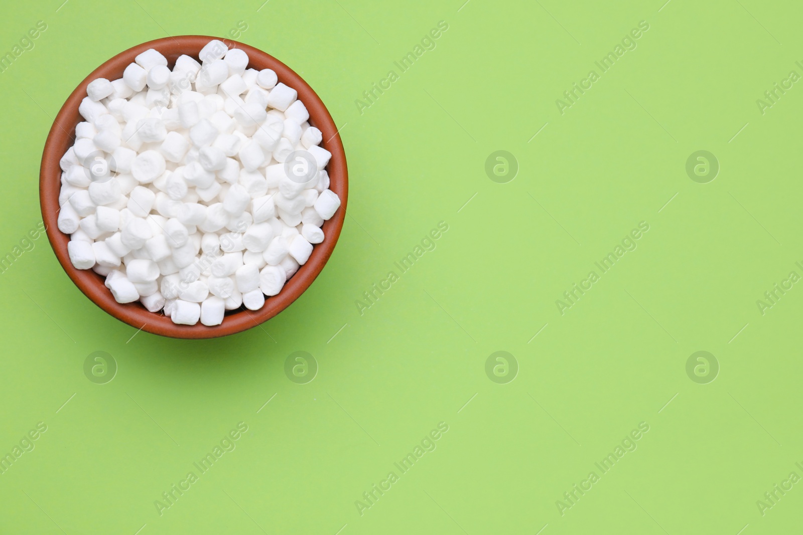 Photo of Bowl of sweet marshmallows on light green background, top view. Space for text