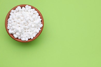 Photo of Bowl of sweet marshmallows on light green background, top view. Space for text