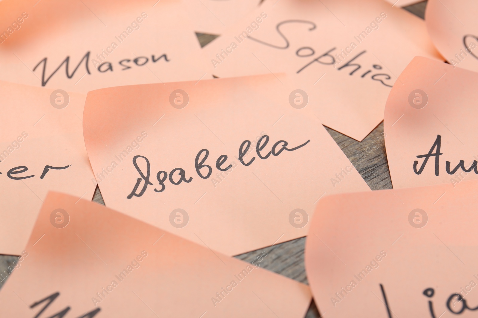 Photo of Paper stickers with different names on wooden table, closeup. Choosing baby's name