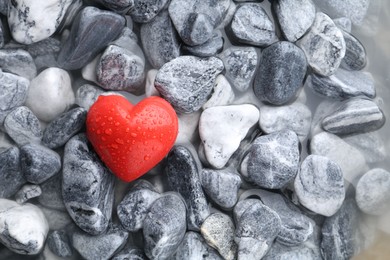 Red decorative heart on stones and water, top view. Space for text