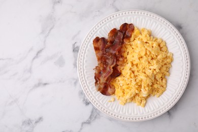Photo of Delicious scrambled eggs with bacon in plate on white marble table, top view. Space for text