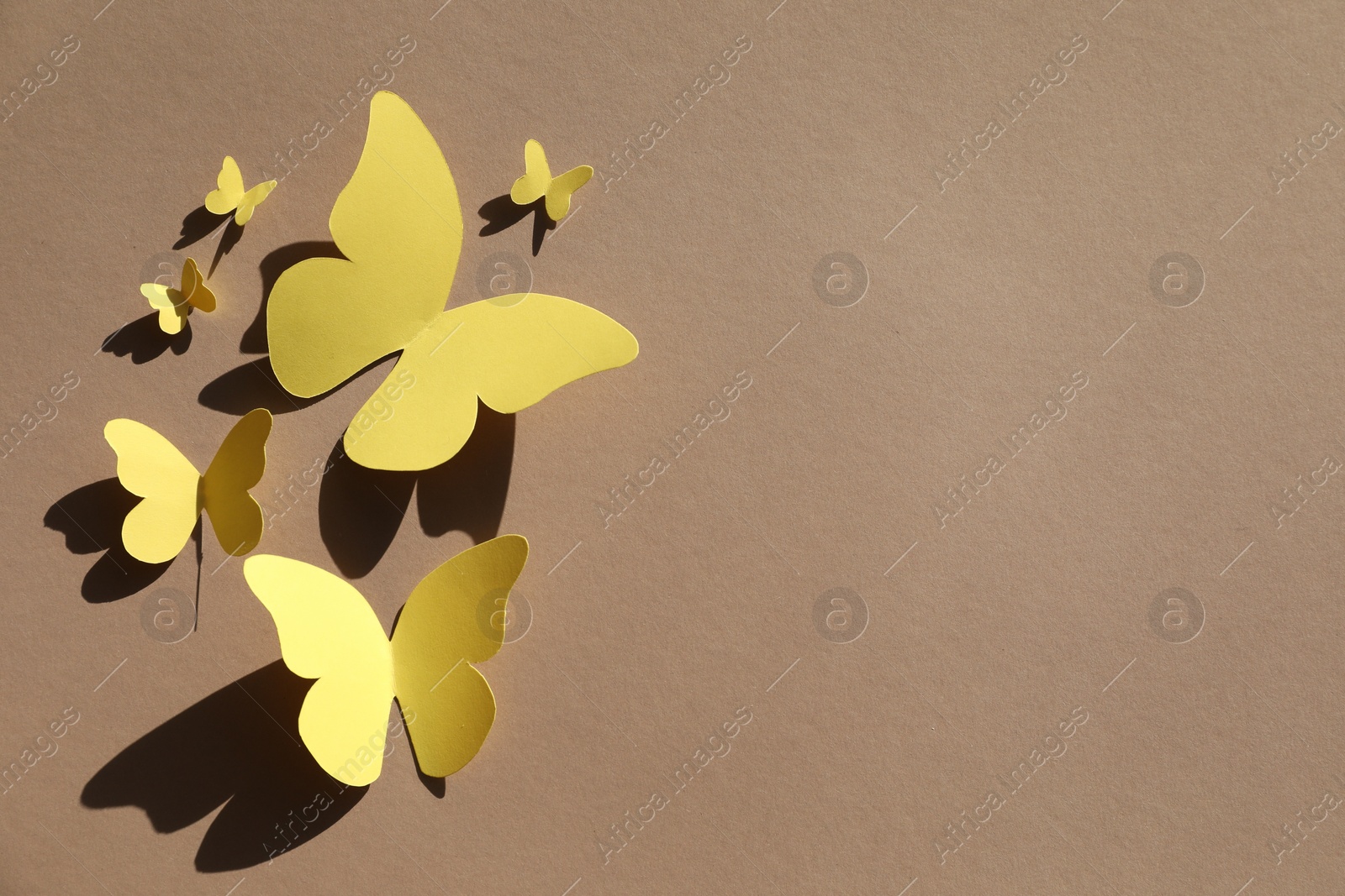 Photo of Yellow paper butterflies on light brown background, top view. Space for text