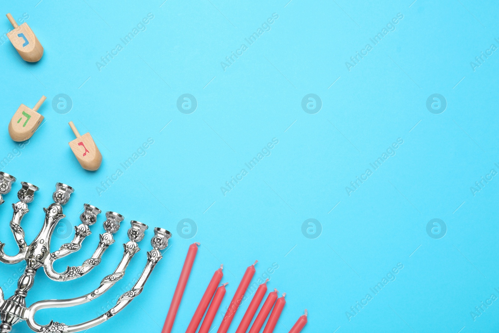 Photo of Silver menorah, red candles and Hanukkah dreidels with Nun, He, Gimel symbols on blue background, flat lay. Space for text