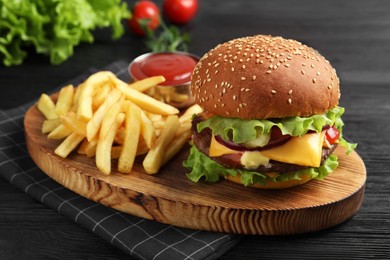 Delicious burger with beef patty, tomato sauce and french fries on dark table