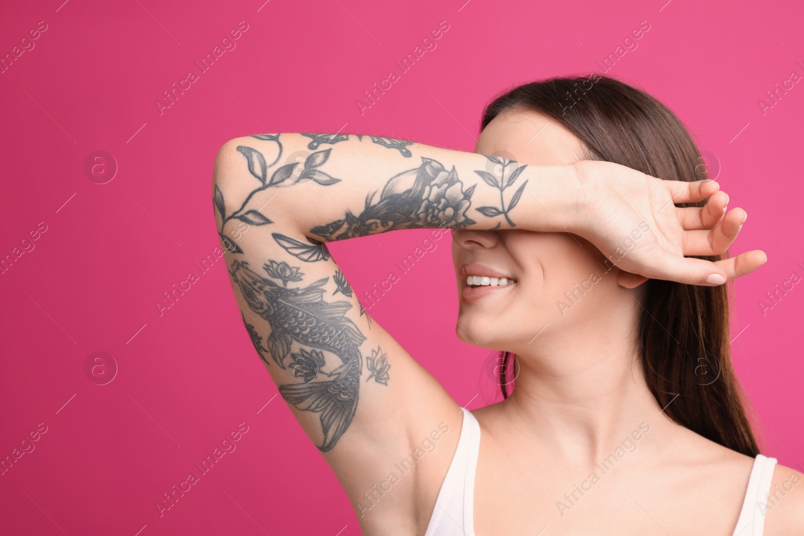 Photo of Beautiful woman with tattoos on arm against pink background