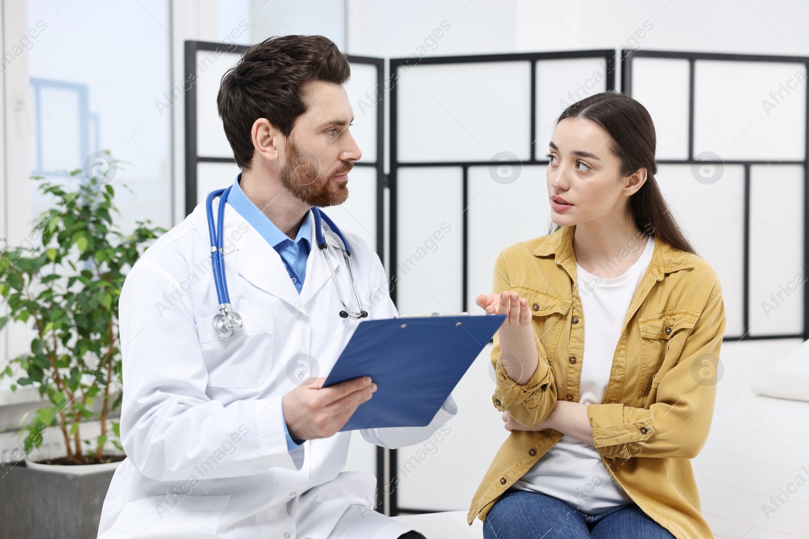 Photo of Doctor with clipboard consulting patient during appointment in clinic